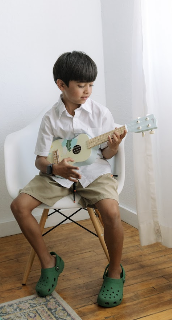 A child seated on a chair playing a ukulele during an In Harmony Music private lesson