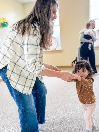 Mom and preschooler are dancing together in class and mom and baby are dancing together in the background
