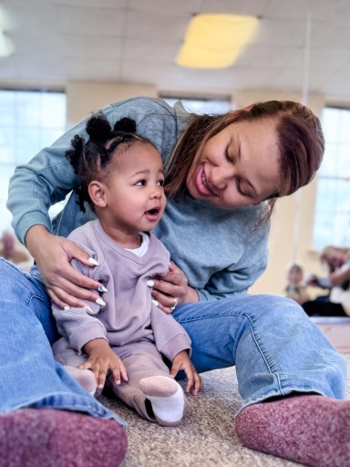 Toddler observing singing and dancing in class from the comfort of her mom's lap