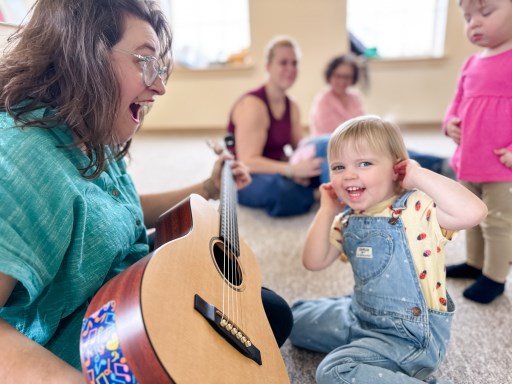 Music teacher singing and playing guitar while preschooler delights in listening