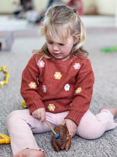 Preschooler playing with wooden frog percussion instrument called a guiro
