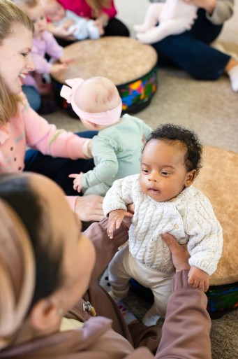 New moms joyfully bouncing their newborns on their shins in music class