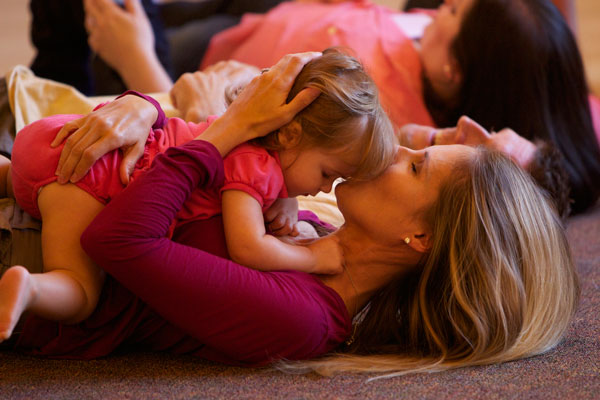 Mom lying on the floor, kissing a young toddler on the head