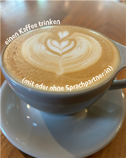 Beautiful latte art in a coffee cup with German text 'einen Kaffee trinken (mit oder ohne Sprachpartner:in)' - having coffee with or without a language partner